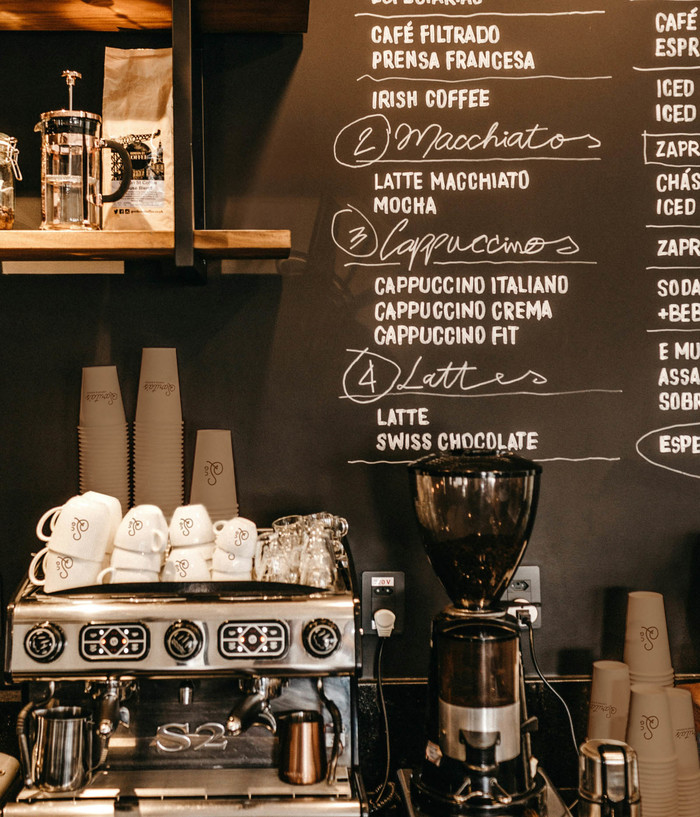 Porcelain and to-go coffee cups stacked on an espresso machine next to a chalkboard menu.