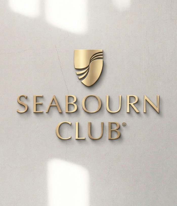 metallic gold logo on a textured light gray surface. Features a stylized gold shield icon split by curved wave lines above the embossed serif text 'SEABOURN CLUB' with a registered trademark symbol.