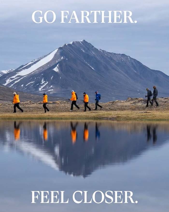 Hikers in orange jackets walk by a still lake perfectly mirroring them and a massive, snow-patched mountain. Text overlays read "GO FARTHER." at the top and "FEEL CLOSER." at the bottom