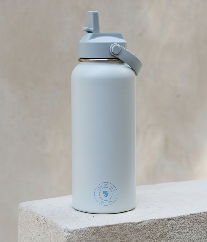 A light blue insulated water bottle with a straw lid stands on a concrete block. Near the base, it features a circular blue logo reading 'SEABOURN CLUB DIAMOND' surrounding a central shield emblem.