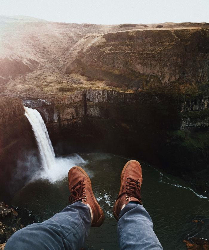 View of a large waterfall with photographer's legs sticking out into the void