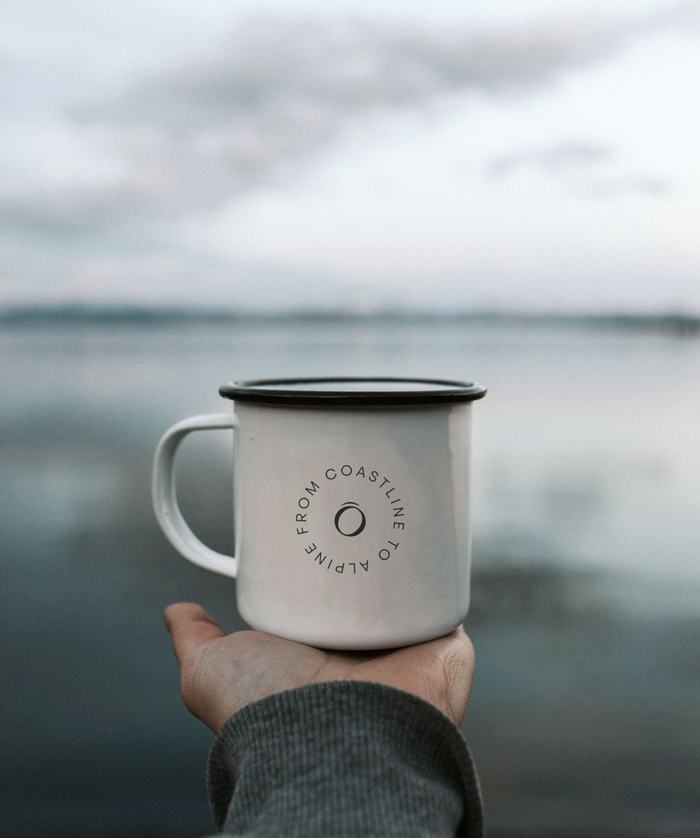 The Overland branded mug held out at arms length with out of focus water feature in background